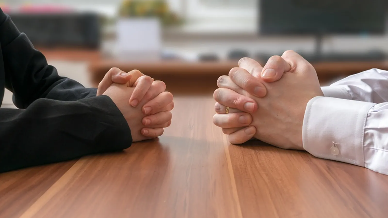 Deux paires de mains jointes face à face sur une table de réunion en bois