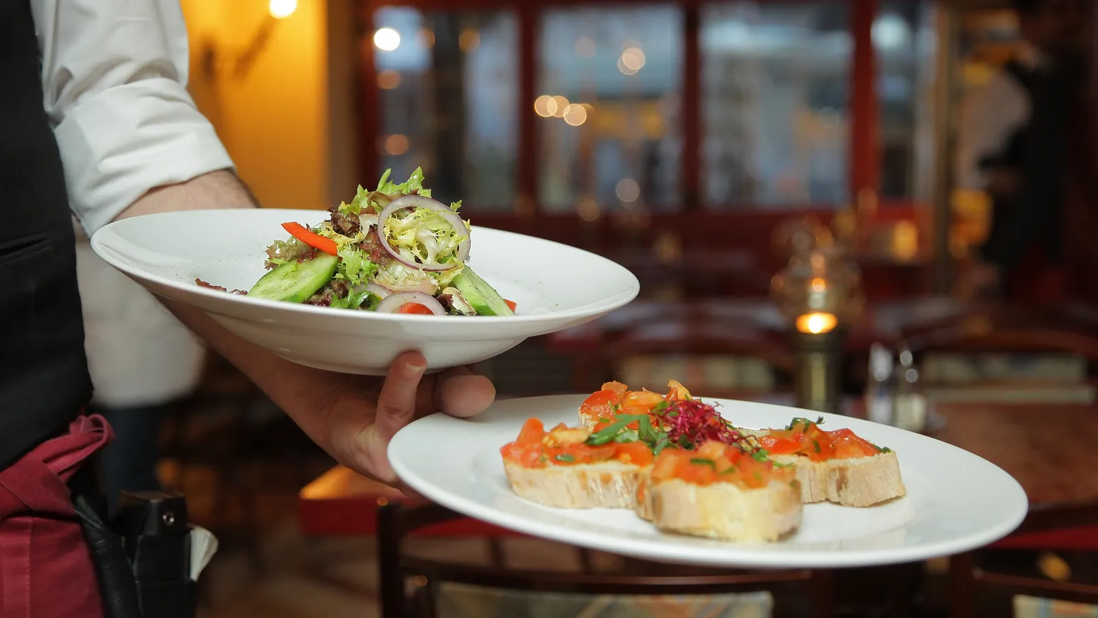 Serveur en salle portant deux assiettes, une salade et des toasts garnis