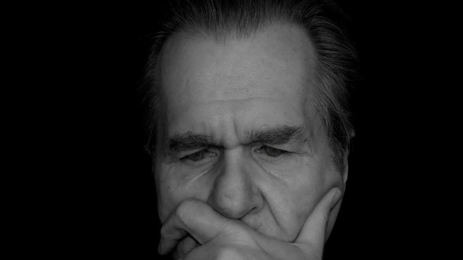 Portrait en noir et blanc d'un homme soucieux, la main posée devant la bouche