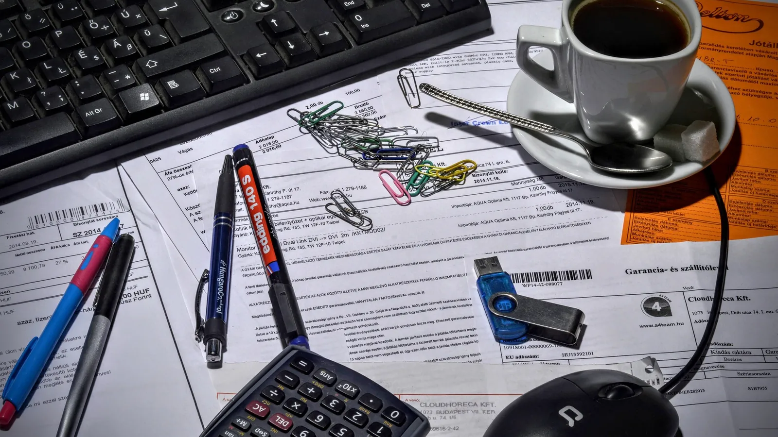 Bureau encombré de factures, trombones, calculatrice et tasse de café près d'un clavier