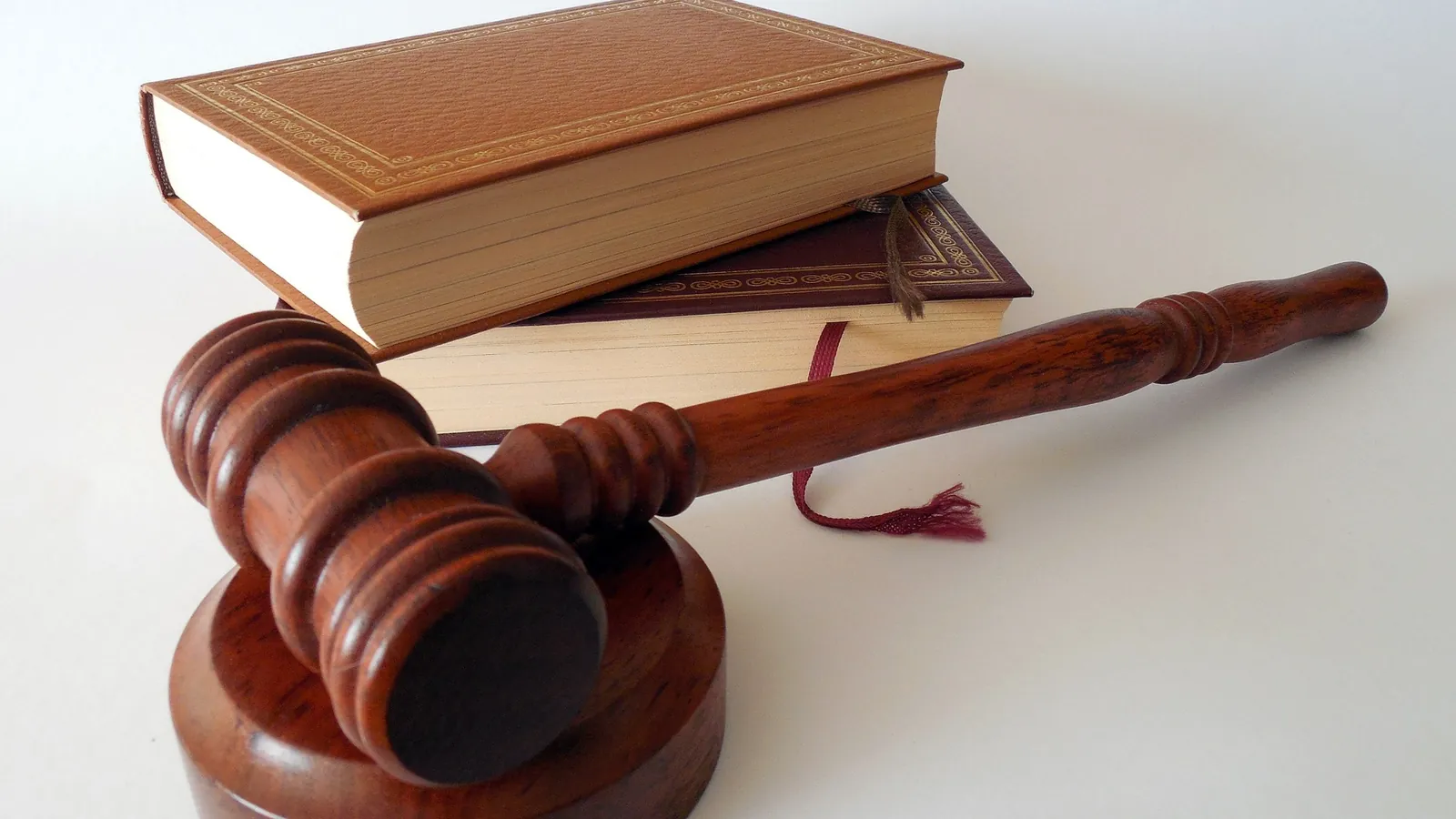 Marteau de juge en bois posé devant deux livres reliés sur un fond clair